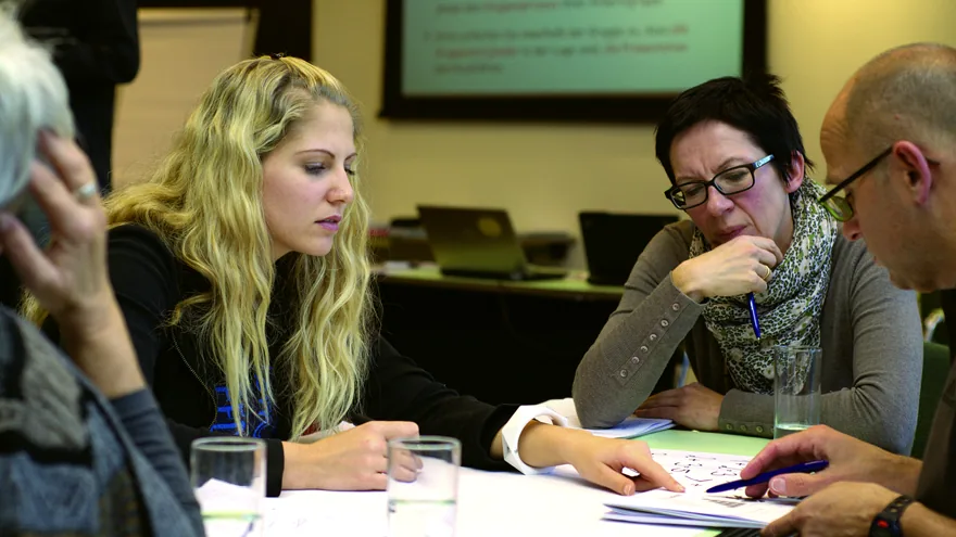 Quatre adultes réunis autour d’une table de travail, en pleine discussion.