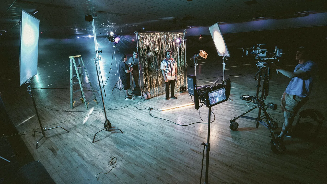 Plateau de tournage éclairé par des projecteurs, avec une caméra sur pied et une équipe technique au travail.